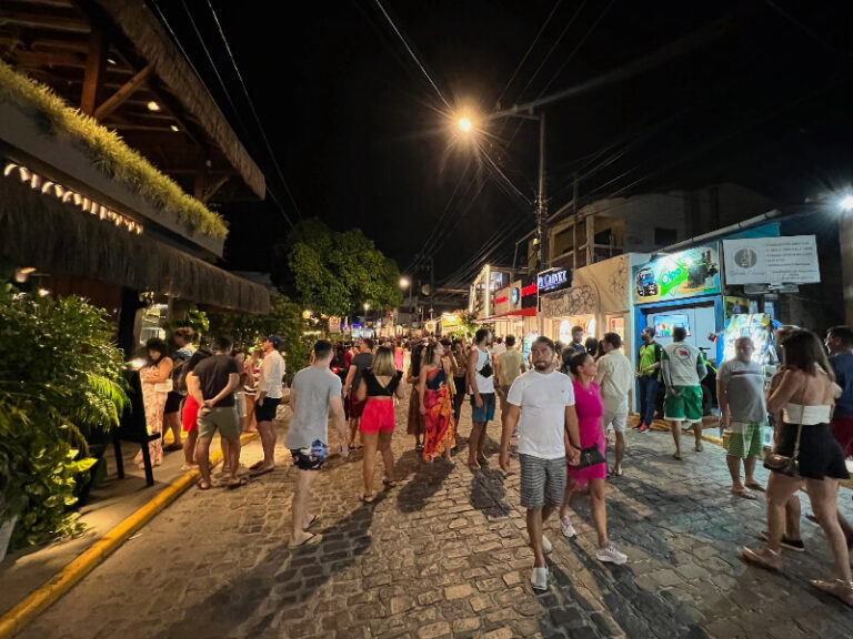 Avenida Baía dos Golfinhos em Pipa à noite com pessoas passeando.