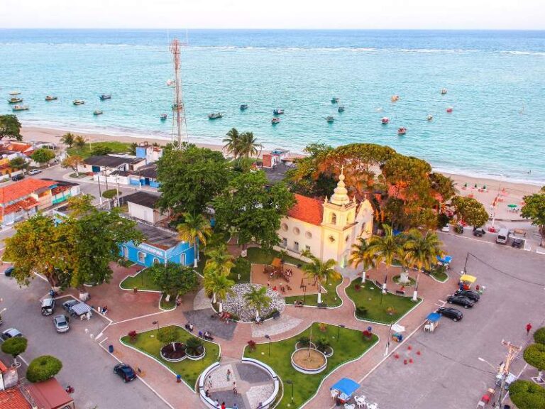 Vista aérea da praça e igreja de São José da Coroa Grande com barcos e mar ao fundo