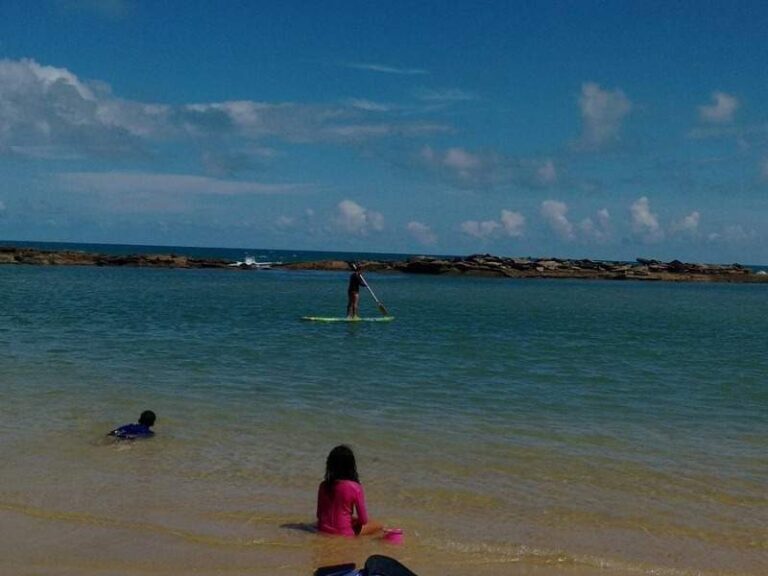Stand-up paddle em águas tranquilas com rochas ao fundo na Praia de Camurupim