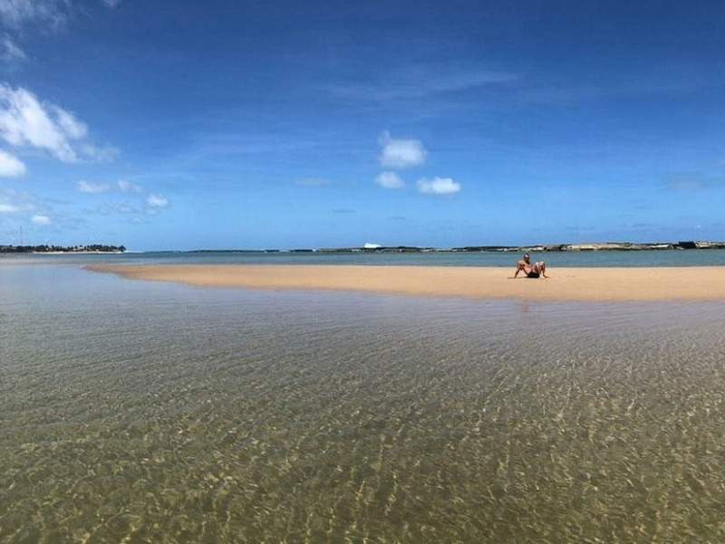 Casal relaxando em banco de areia na serena Praia de Camurupim sob céu azul