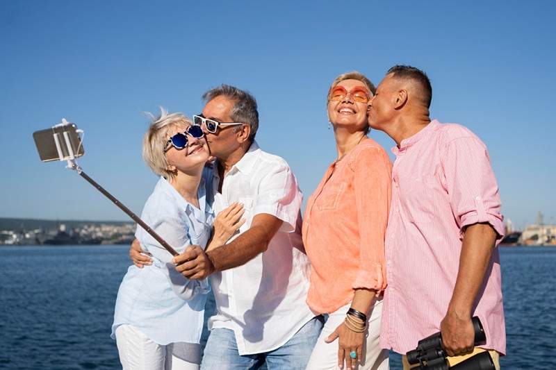 Casais sêniores alegres tirando uma selfie à beira-mar, desfrutando do turismo sênior