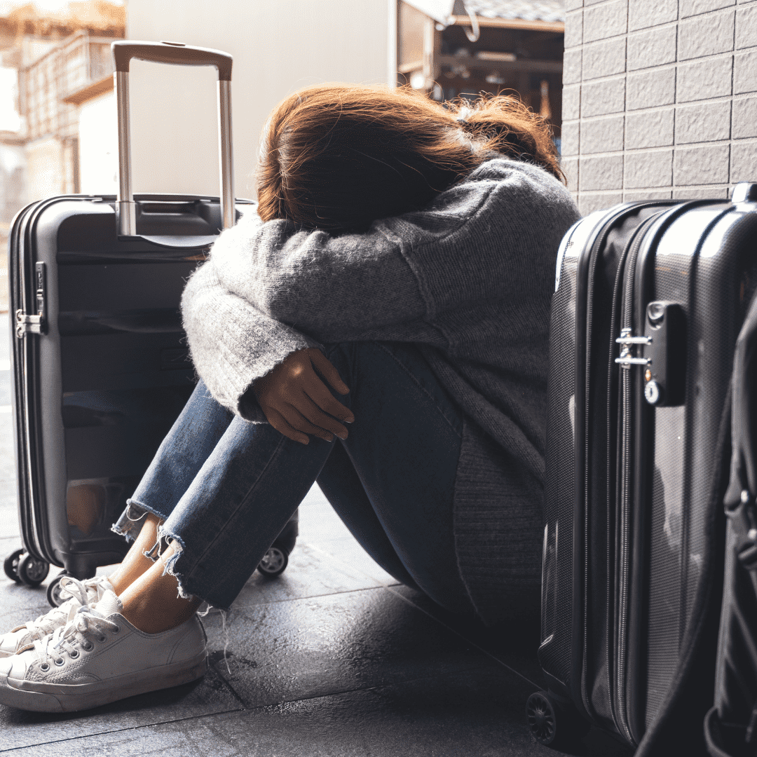 Mulher sentada no chão entre malas, com a cabeça apoiada nos braços, demonstrando frustração durante a viagem