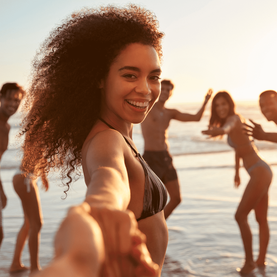Grupo de amigos se diverte na praia durante o pôr do sol, sorrindo e de mãos dadas na água