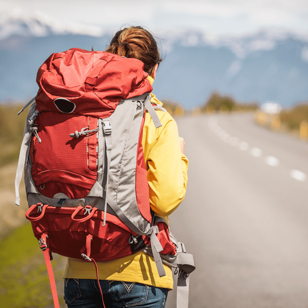 Pessoa com mochila de viagem caminha por estrada rumo às montanhas, simbolizando aventura e liberdade