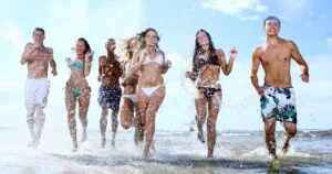 Grupo de jovens sorridentes correndo pela praia, essência de viagens em grupo harmoniosas.