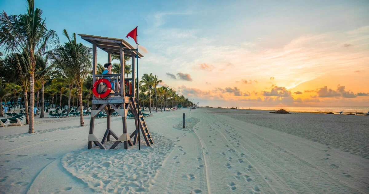 Praia nordestina ao pôr do sol com barraca de salva-vidas e dicas de segurança no Brasil.