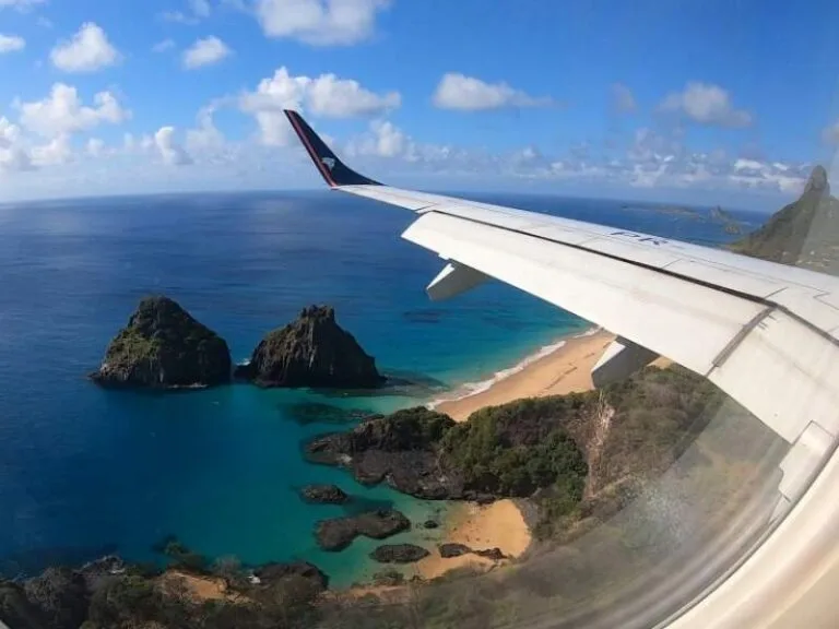 Asa de avião sobrevoando a paisagem icônica dos Dois Irmãos em Fernando de Noronha