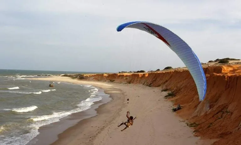 Parapentista em voo sobre as falésias e o mar de Canoa Quebrada